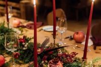 a boho winter wedding tablescape with an evergreen and red rose runner, feathers and burgundy candles, burgundy napkins and pomegranates