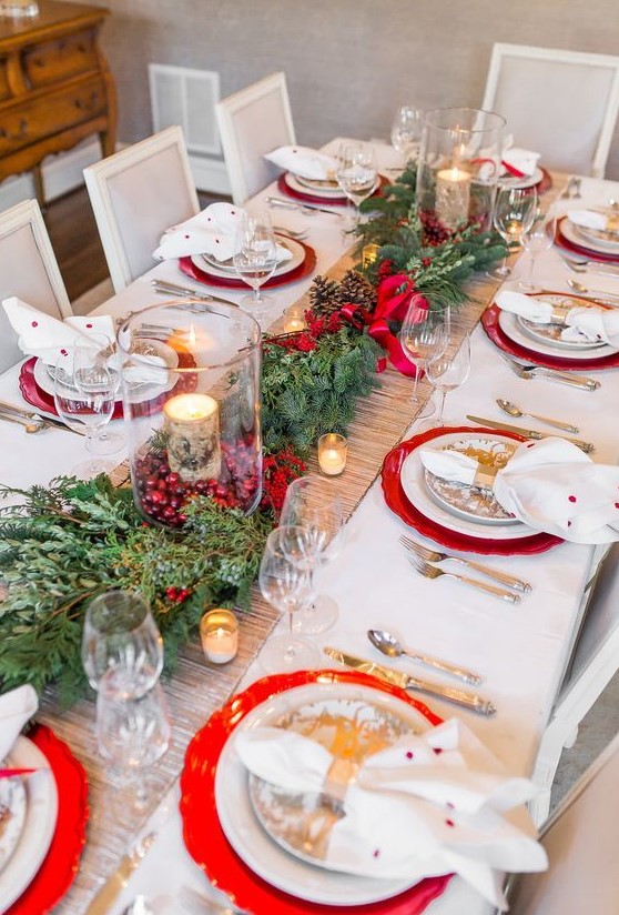 a bright Christmas wedding table with red chargers, an vergreen and pinecone runner, cranberries and birch bark candles, printed plates and polka dot napkins