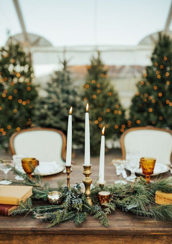 a chic lush table runner of evergreens, candles, tall and thin candles in a candelabra, vintage books for a Christmas wedding