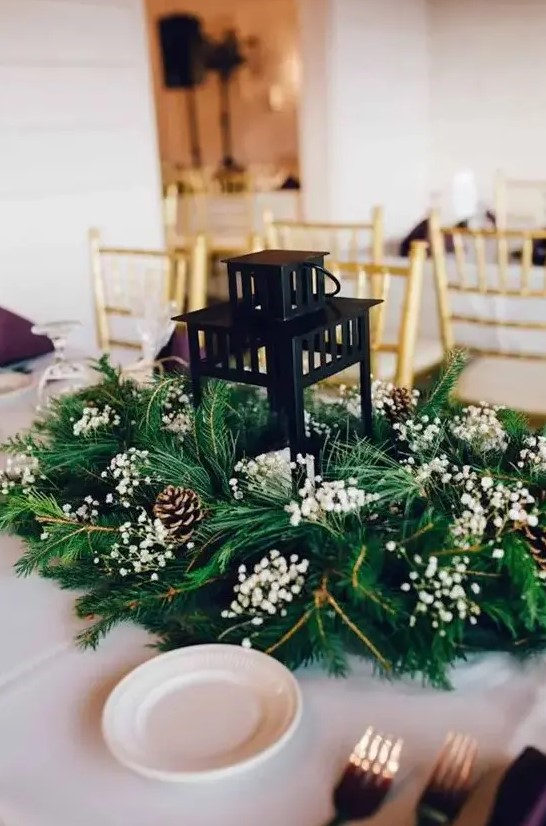 a classy winter wedding centerpiece of evergreens, baby's breath, pinecones and a candle lantern in the center is amazing