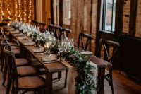 a cozy winter wedding tablescape with a lush evergreen table runner and candle lanterns is amazing for winter and Christmas