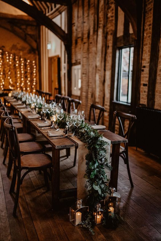 a cozy winter wedding tablescape with a lush evergreen table runner and candle lanterns is amazing for winter and Christmas