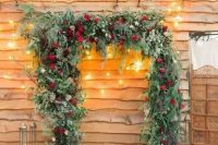 a gorgeous Christmas wedding arch shaped as a frame, covered with evergreens, greenery, red roses and with lots of candle lanterns around
