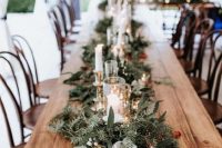 a lush and textural table runner with evergreens and greenery, candles and lights and some bold berries is adorable for winter