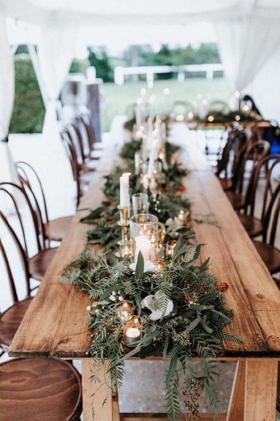 a lush and textural table runner with evergreens and greenery, candles and lights and some bold berries is adorable for winter