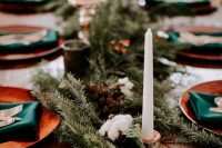 a lush winter wedding table runner with pinecones and cotton and tall and thin candles is a cool idea for a winter wedding