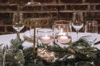a refined winter wedding centerpiece of evergreens and floating candles plus gold calligraphy is a very chic idea