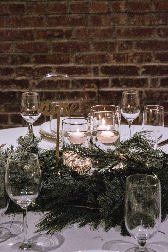 a refined winter wedding centerpiece of evergreens and floating candles plus gold calligraphy is a very chic idea