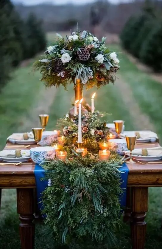 a rustic evergreen table runner with berries and pinecones and lots of candles bring winter spirit