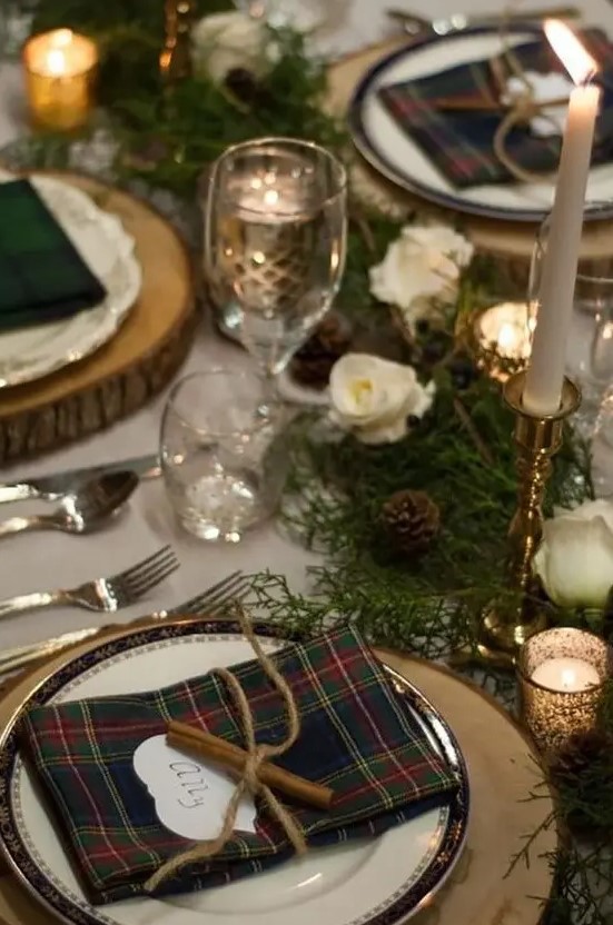 a rustic winter wedding table setting with plaid napkins, cinnamon, evergreens, white blooms and pinecones