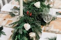 a simple and cozy winter chalet wedding tablescape with an uncovered table, an evergreen table runner, berry and white rose table runner and tall candles