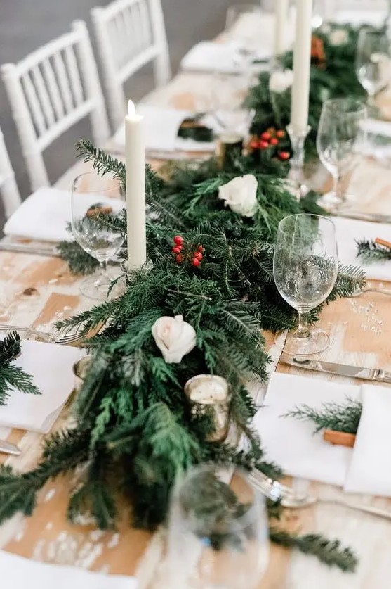 a simple and cozy winter chalet wedding tablescape with an uncovered table, an evergreen table runner, berry and white rose table runner and tall candles