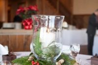 a simple rustic Christmas centerpiece of a wood slice, evergreens, berries, pinecones and candle lanterns