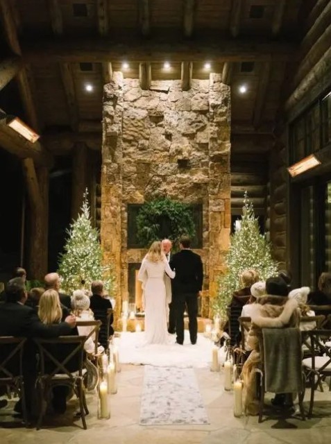a stone fireplace, candles, an evergreen wreath and a couple of lit up Christmas trees on the sides is a great idea for a holiday wedding