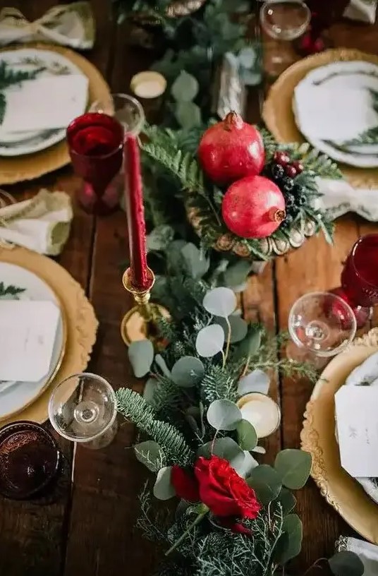 a winter wedding tablescape with a greenery and fir runner, pomegranates and berries, red candles and gold chargers