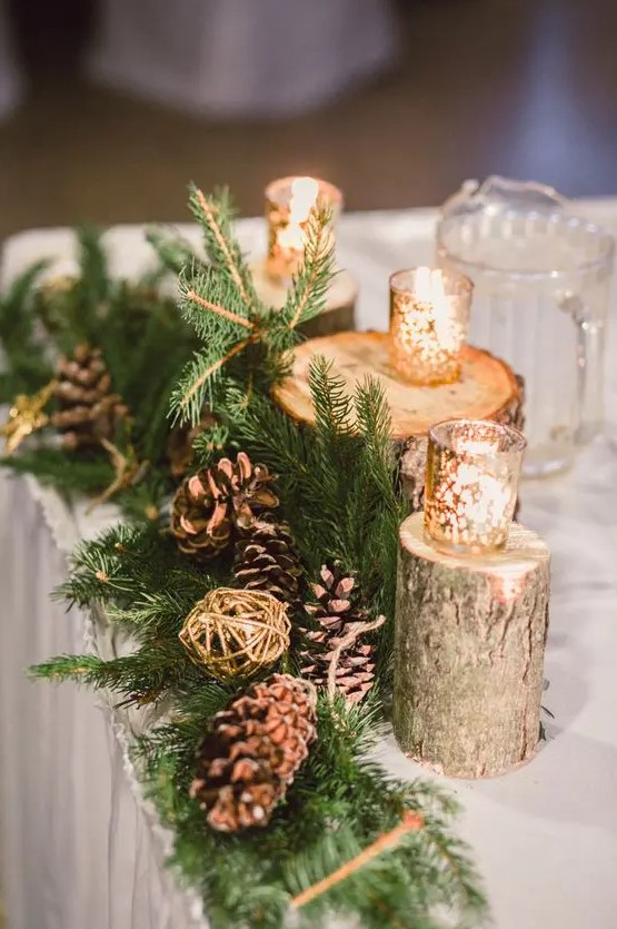 a woodland winter wedding centerpiece of evergreens, pinecones, gilded yarn balls and candleholders on tree stumps