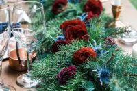an evergreen table runner with bold burgundy blooms and thistles for a rustic winter wedding