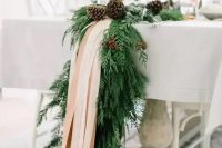 an exquisite winter table runner of evergreens, pinecones and blush ribbons will fit even the most refined winter wedding and will give it a cozy feel