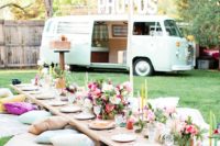 04 a boho chic picnic with a table on the grass, pillows and blankets and bold florals