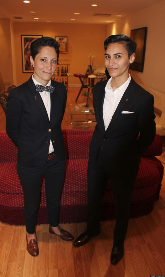 both brides wearing the same black pantsuits, loafers and a bow tie look very cohesive and elegant together