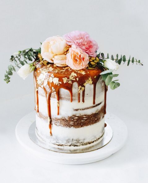 dirty frosted wedding cake with caramel drip and lush pastel flowers and greenery
