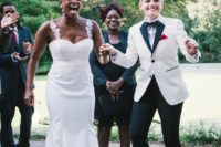 one bride wearing black pants, a white and black jacket, a bow tie, the second bride wearing a mermaid wedding dress with lace straps