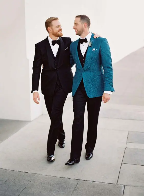 both grooms in stylish tuxedos, one of them wearing a patterned turquoise jacket