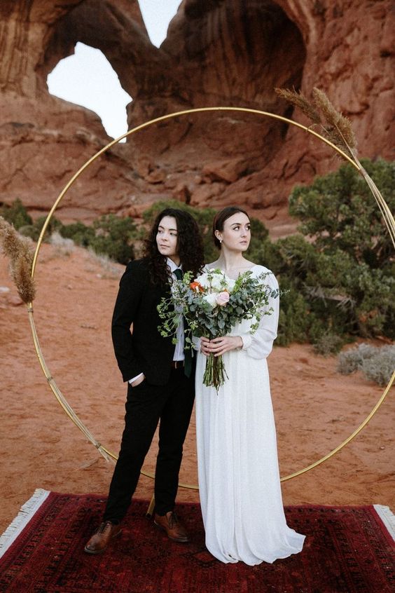 a black pantsuit, a white shirt and a black tie, brown shoes, a romantic plain wedding dress with long sleeves for a desert wedding