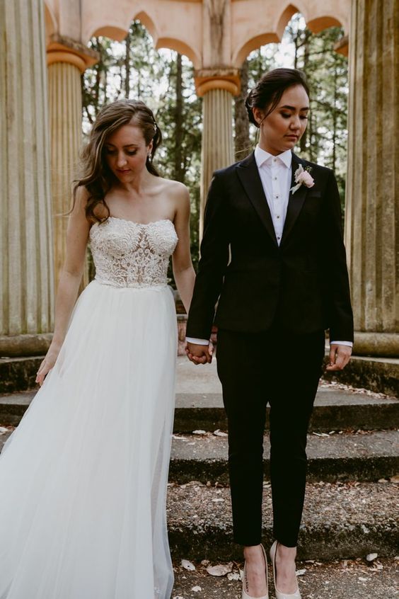 a black pantsuit with cropped pants, a white shirt and a boutonniere, a strapless A-line wedding dress with a lace bodice and a pleated skirt