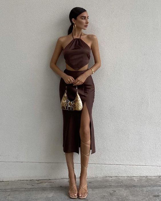 A brown two piece dress with a crop top and a midi skirt with a slit, lace up shoes, a gold baguette bag and hoop earrings