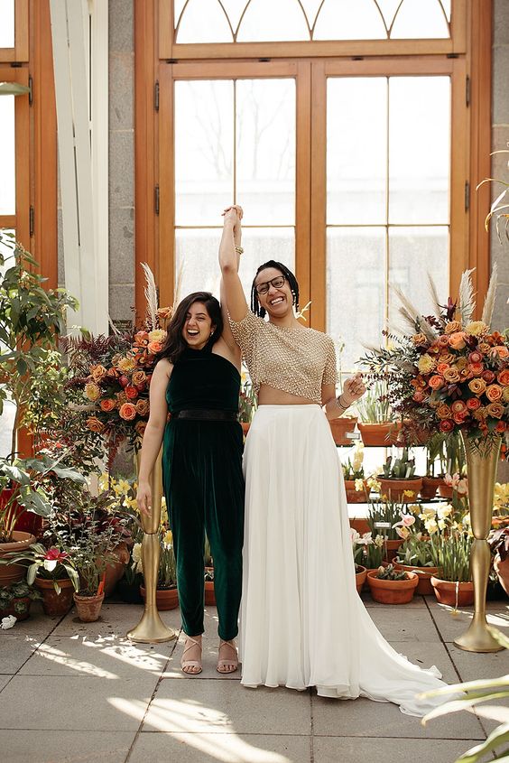 a dark green halter neckline jumpsuit, nude lace up shoes for one bride, a separate with a beaded crop top and a pleated skirt with a train for the second bride