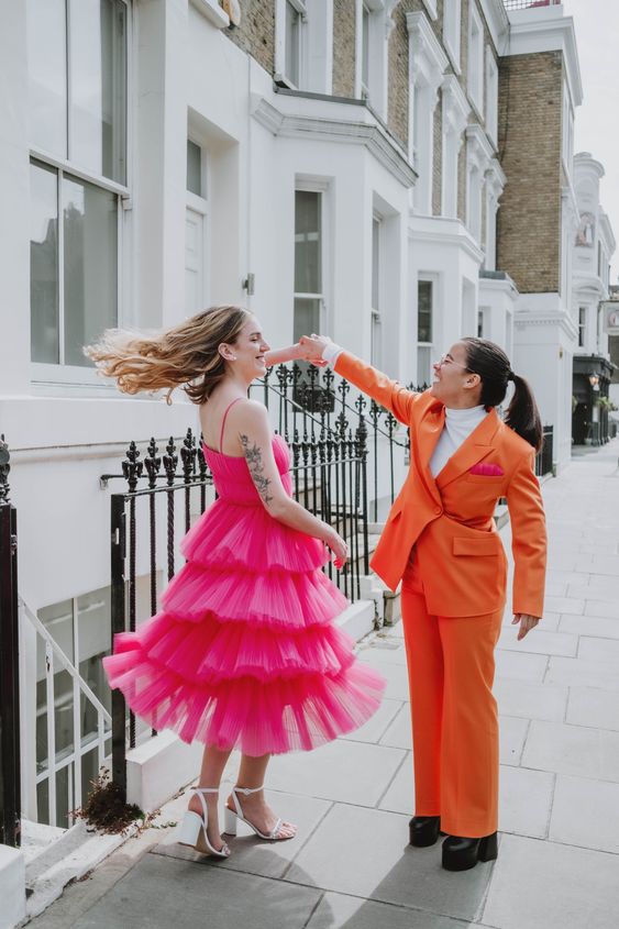 a hot pink ruffle wedding dress with spaghetti straps, white shoes, an orange pantsuit with a white turtleneck for a colorful wedding