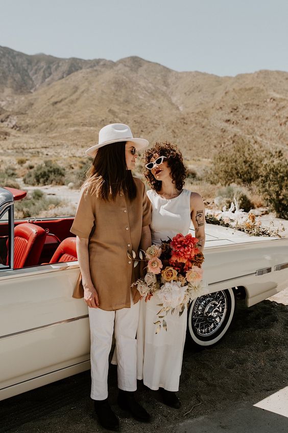 a plain sleeveless midi wedding dress paired with black boots, white pants, a beige overiszed shirt and boots plus a hat for a desert boho wedding