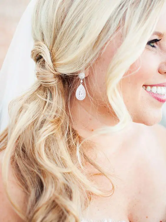 a pretty and easy blonde knot side pnytail and waves framing the face are a simple and cool idea for a wedding