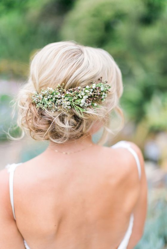 a romantic wavy side updo with a volume on top and a fresh flower and greenery hairpiece for a natural feel