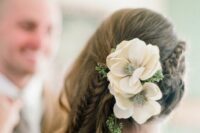 a side swept hairstyle with a side braid and waves down accented with greenery and white blooms is a lovely idea