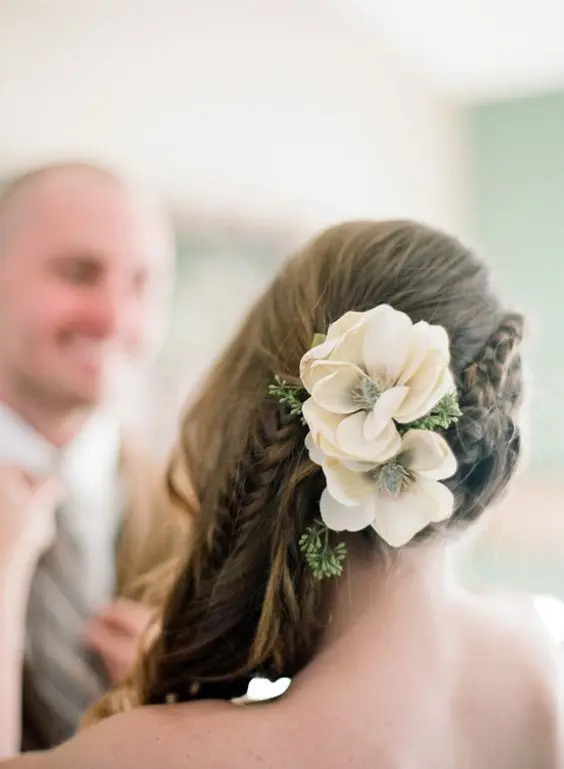 a side swept hairstyle with a side braid and waves down accented with greenery and white blooms is a lovely idea