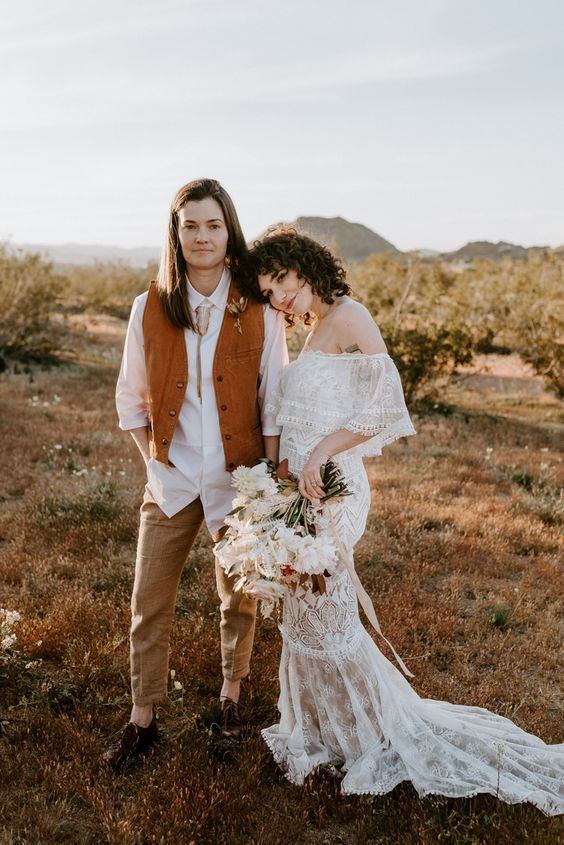 boho bridal looks with a white shirt, an orange waistcoat, tan pants, brown shoes, an off the shoulder lace mermaid wedding dress with a train