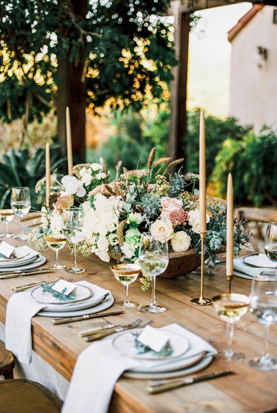 beautiful rustic table setting with an uncovered table and a neutral flower centerpiece