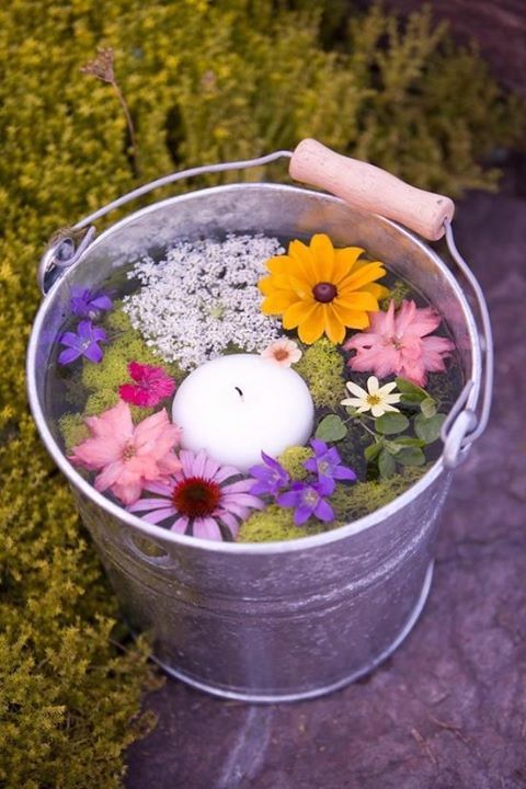a galvanized bucket with flowers and a floating candle