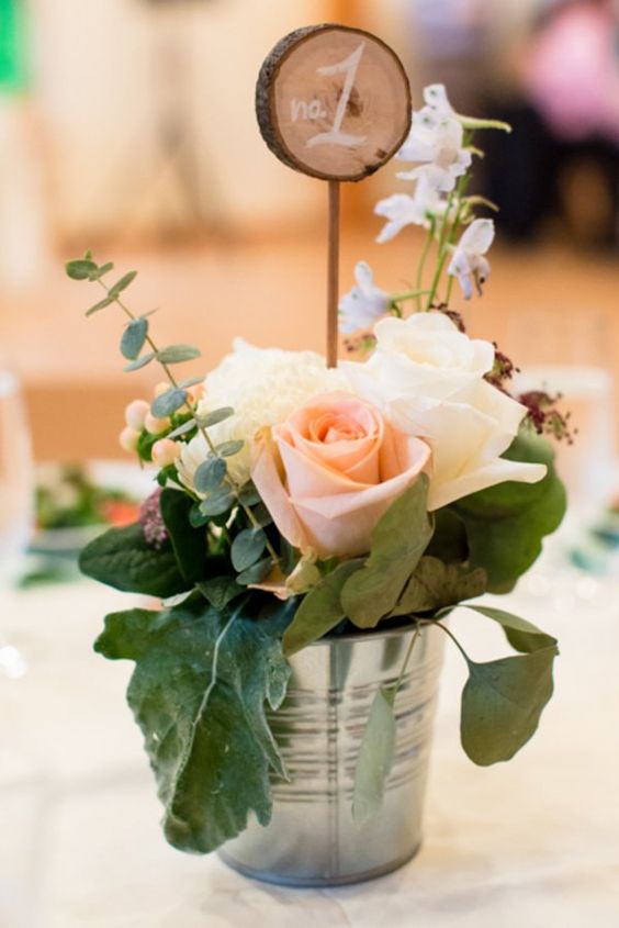 galvanized bucket with blush roses and leaves and a wood slice table number