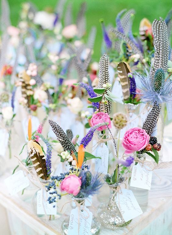 escort cards attached to the vases with feathers and flowers