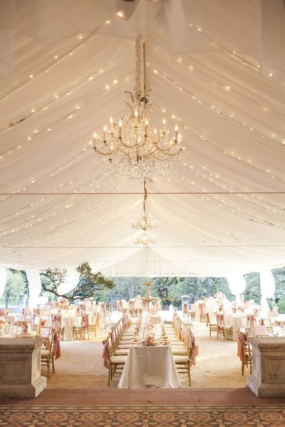 neutral wedding tent with a lot of lights and chandeliers
