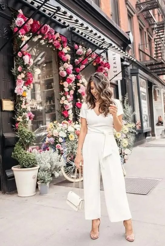 a casual white jumpsuit with a V-neckline, short sleeves, wideleg pants, nude shoes and a white bag