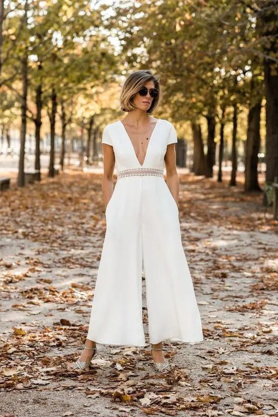 a chic modern white jumpsuit with wideleg pants and pockets, a plunging neckline, short sleeves and silver shoes