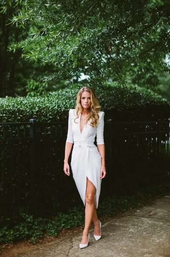 a gorgeous modern white dress with sculptural shoulders, a plunging neckline, a slit plus white heels