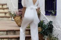a plain white jumpsuit plus a sheer organza top with puff sleeves and a bow are a cool combo for a bridal shower or a wedding