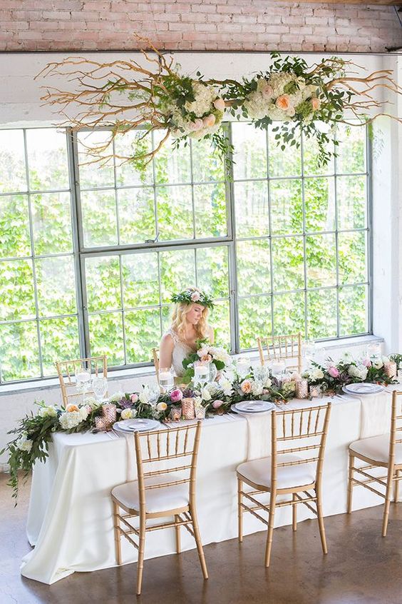 wedding reception with a lush floral table runner and a cool floral hanging over the table