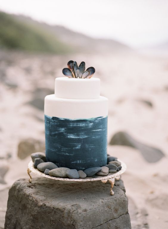 a watercolor navy wedding cake topped with mussel shells