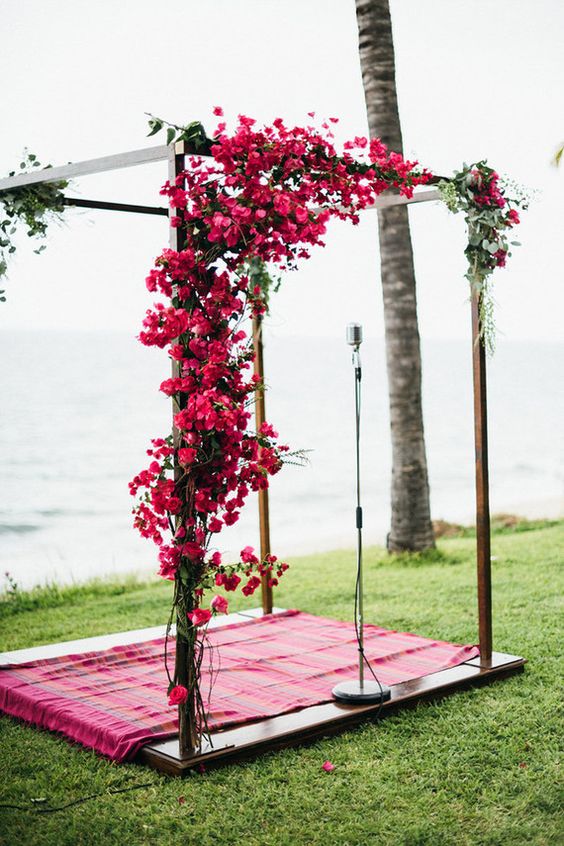 a bold tropical wedding arch decorated with fuchsia flowers